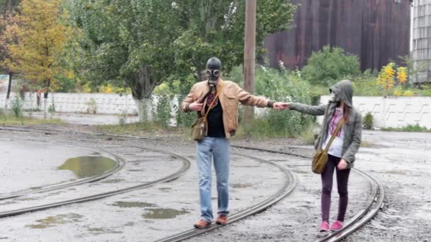 The guy with the girl in gas-helmets walk on rails — Stock Video