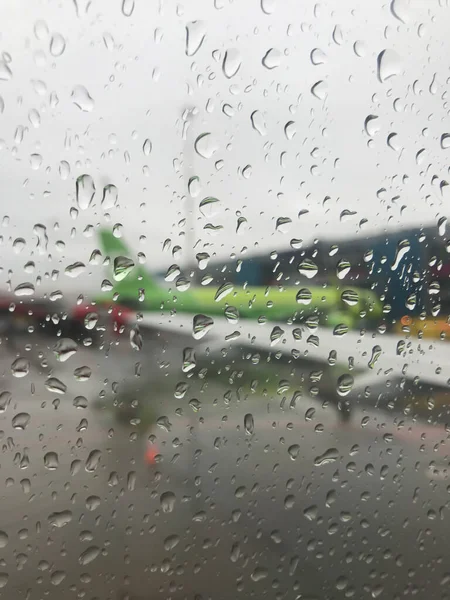 The blurred wing of the plane is visible through a drop of rain on the window of the aircraft