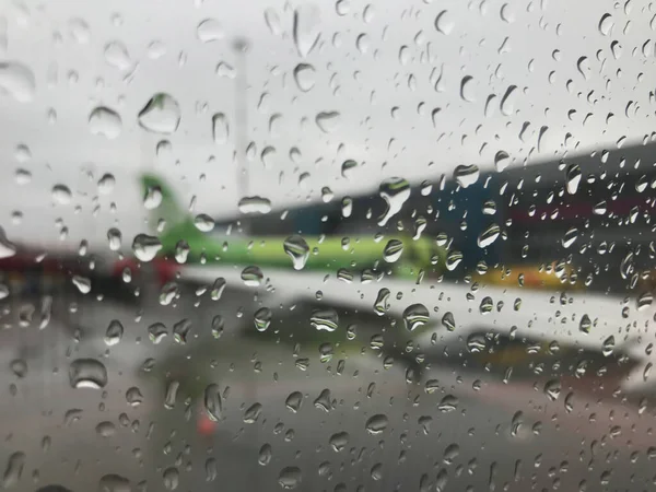 The blurred wing of the plane is visible through a drop of rain on the window of the aircraft