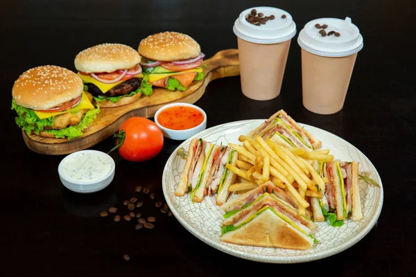 A delicious sandwich made with white bread, tomatoes, onions, lettuce. Sandwich. Delicious burgers with beef, tomatoes, cheese and salad. Coffee with you and French fries
