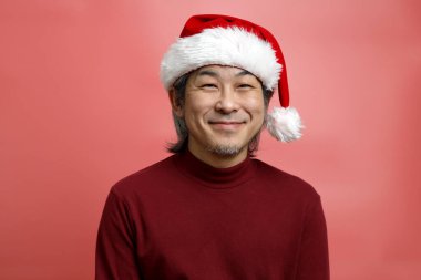 Pembe arka planda Noel Baba şapkalı Asyalı adam portresi..