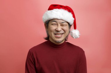 Pembe arka planda Noel Baba şapkalı Asyalı adam portresi..