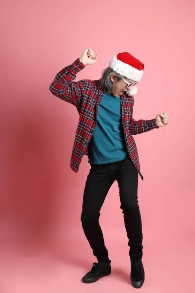 ピンクの背景に立っているクリスマスの帽子を持つシニアアジアの男 — ストック写真