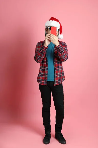 ピンクの背景に立っているクリスマスの帽子を持つシニアアジアの男 — ストック写真