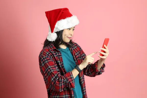 Pembe arka planda duran Noel Baba şapkalı Asyalı kadın..