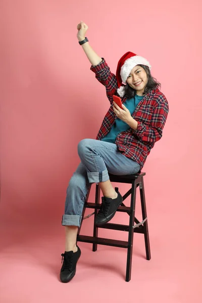 Pembe arka planda duran Noel Baba şapkalı Asyalı kadın..