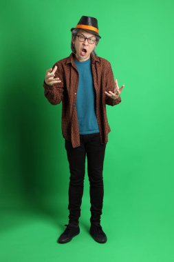 Son sınıf Asyalı adam Şükran Günü renk temalı yeşil arka planda duran turuncu ekose gömlek ve siyah şapka giyiyor..