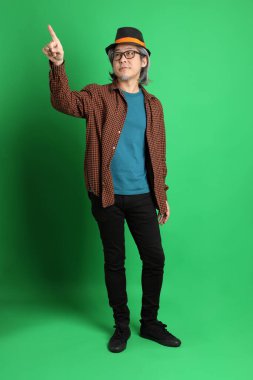 Son sınıf Asyalı adam Şükran Günü renk temalı yeşil arka planda duran turuncu ekose gömlek ve siyah şapka giyiyor..