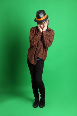 Son sınıf Asyalı adam Şükran Günü renk temalı yeşil arka planda duran turuncu ekose gömlek ve siyah şapka giyiyor..