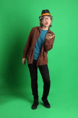 Son sınıf Asyalı adam Şükran Günü renk temalı yeşil arka planda duran turuncu ekose gömlek ve siyah şapka giyiyor..