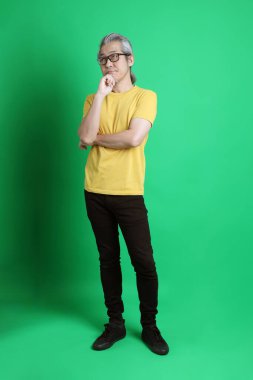 Yeşil arka planda duran uzun gri saçlı yaşlı Asyalı adam..