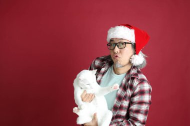 Kıdemli Asyalı adam kırmızı arka planda duran Noel Baba şapkalı kırmızı ekose gömlek giyiyor..