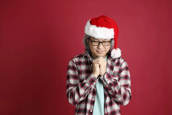 Kıdemli Asyalı Adam Kırmızı Arka Planda Duran Noel Baba Şapkalı — Stok fotoğraf