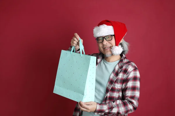 Kıdemli Asyalı Adam Kırmızı Arka Planda Duran Noel Baba Şapkalı — Stok fotoğraf