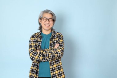 Mavi arka planda duran sarı ekose gömlekli yaşlı Asyalı adam..