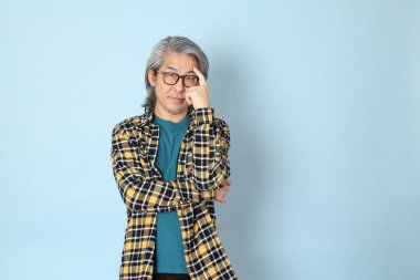 Mavi arka planda duran sarı ekose gömlekli yaşlı Asyalı adam..