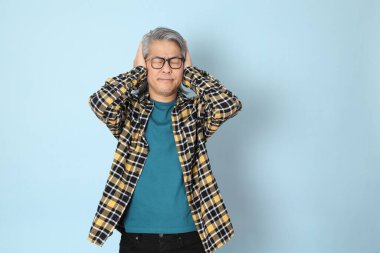 Mavi arka planda duran sarı ekose gömlekli yaşlı Asyalı adam..