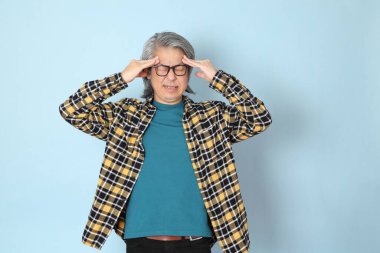 Mavi arka planda duran sarı ekose gömlekli yaşlı Asyalı adam..