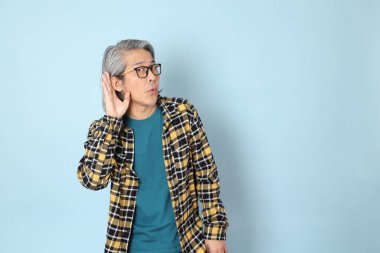 Mavi arka planda duran sarı ekose gömlekli yaşlı Asyalı adam..