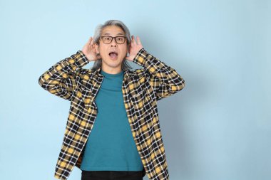 Mavi arka planda duran sarı ekose gömlekli yaşlı Asyalı adam..