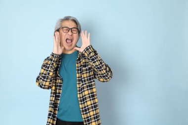 Mavi arka planda duran sarı ekose gömlekli yaşlı Asyalı adam..