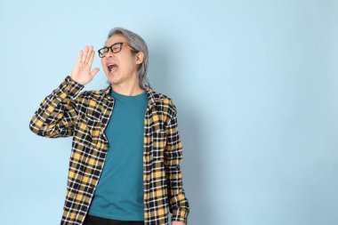 Mavi arka planda duran sarı ekose gömlekli yaşlı Asyalı adam..