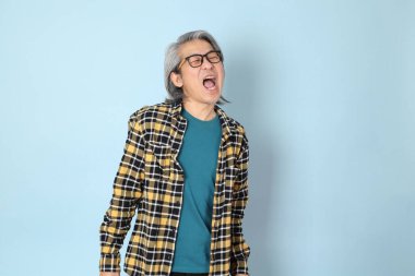 Mavi arka planda duran sarı ekose gömlekli yaşlı Asyalı adam..