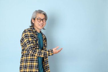 Mavi arka planda duran sarı ekose gömlekli yaşlı Asyalı adam..