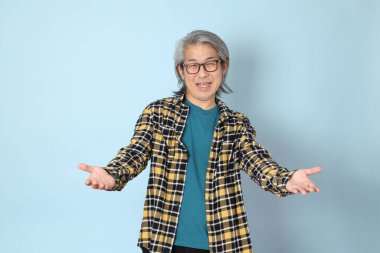 Mavi arka planda duran sarı ekose gömlekli yaşlı Asyalı adam..