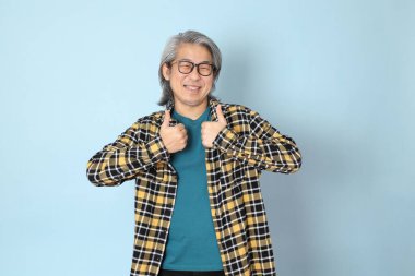 Mavi arka planda duran sarı ekose gömlekli yaşlı Asyalı adam..