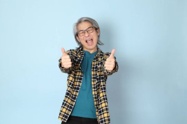 Mavi arka planda duran sarı ekose gömlekli yaşlı Asyalı adam..