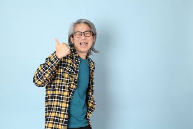 Mavi arka planda duran sarı ekose gömlekli yaşlı Asyalı adam..