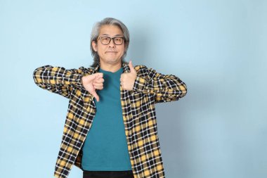 Mavi arka planda duran sarı ekose gömlekli yaşlı Asyalı adam..