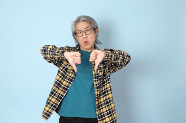 Mavi arka planda duran sarı ekose gömlekli yaşlı Asyalı adam..