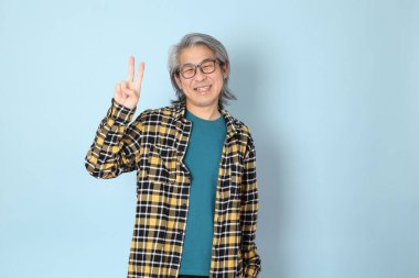 Mavi arka planda duran sarı ekose gömlekli yaşlı Asyalı adam..