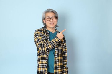 Mavi arka planda duran sarı ekose gömlekli yaşlı Asyalı adam..