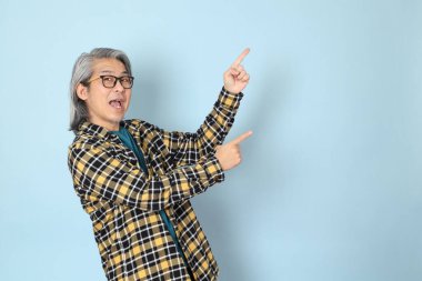 Mavi arka planda duran sarı ekose gömlekli yaşlı Asyalı adam..