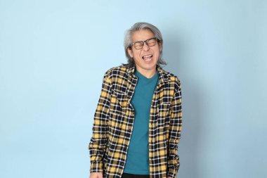 Mavi arka planda duran sarı ekose gömlekli yaşlı Asyalı adam..