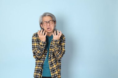 Mavi arka planda duran sarı ekose gömlekli yaşlı Asyalı adam..