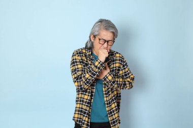 Mavi arka planda duran sarı ekose gömlekli yaşlı Asyalı adam..