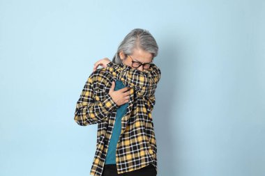 Mavi arka planda duran sarı ekose gömlekli yaşlı Asyalı adam..