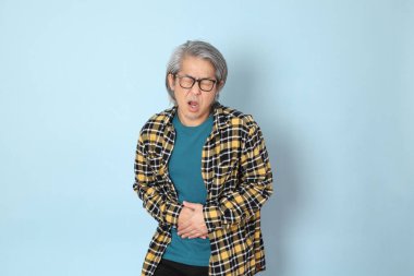 Mavi arka planda duran sarı ekose gömlekli yaşlı Asyalı adam..
