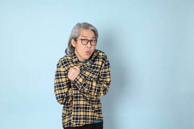 Mavi arka planda duran sarı ekose gömlekli yaşlı Asyalı adam..