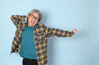 Mavi arka planda duran sarı ekose gömlekli yaşlı Asyalı adam..