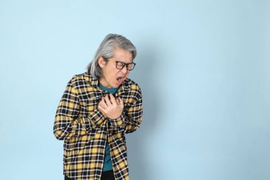 Mavi arka planda duran sarı ekose gömlekli yaşlı Asyalı adam..