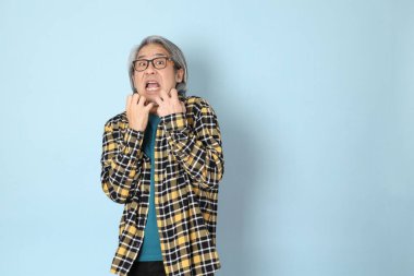 Mavi arka planda duran sarı ekose gömlekli yaşlı Asyalı adam..