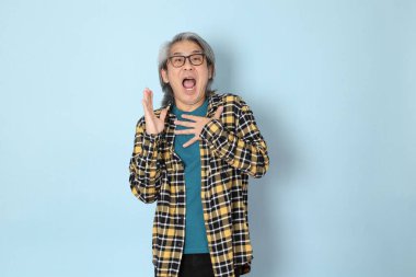 Mavi arka planda duran sarı ekose gömlekli yaşlı Asyalı adam..