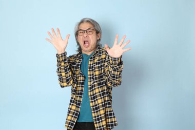 Mavi arka planda duran sarı ekose gömlekli yaşlı Asyalı adam..