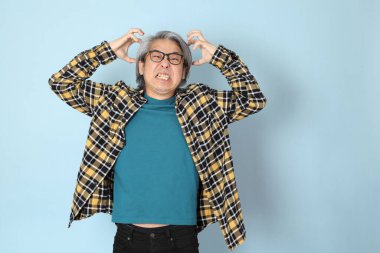 Mavi arka planda duran sarı ekose gömlekli yaşlı Asyalı adam..