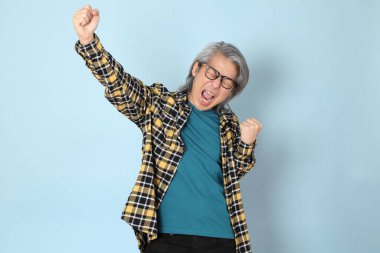 Mavi arka planda duran sarı ekose gömlekli yaşlı Asyalı adam..